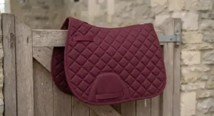 A burgundy low-cost GP saddle pad numnah hanging on a stable door.